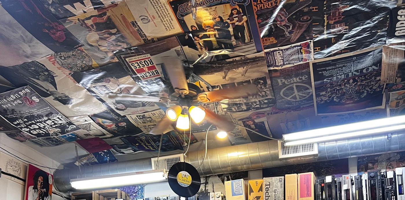 The shop ceiling covered edge to edge in old concert posters and album sleeves, with a record hanging from a cord.