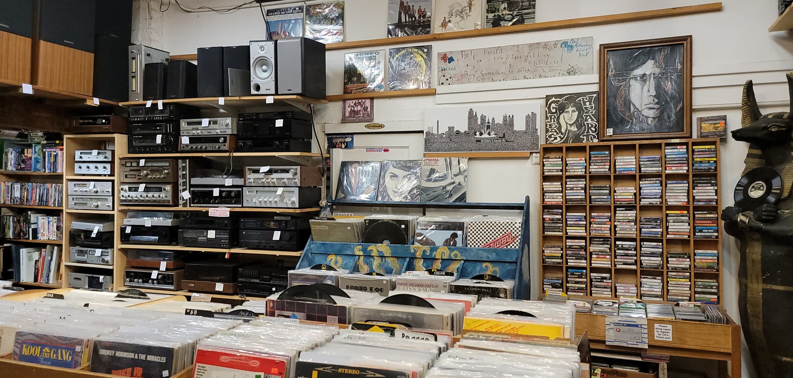 Inside It's A Beautiful Day: shelves of vintage stereo receivers and tape decks above a wall of cassettes, with vinyl bins in the foreground.