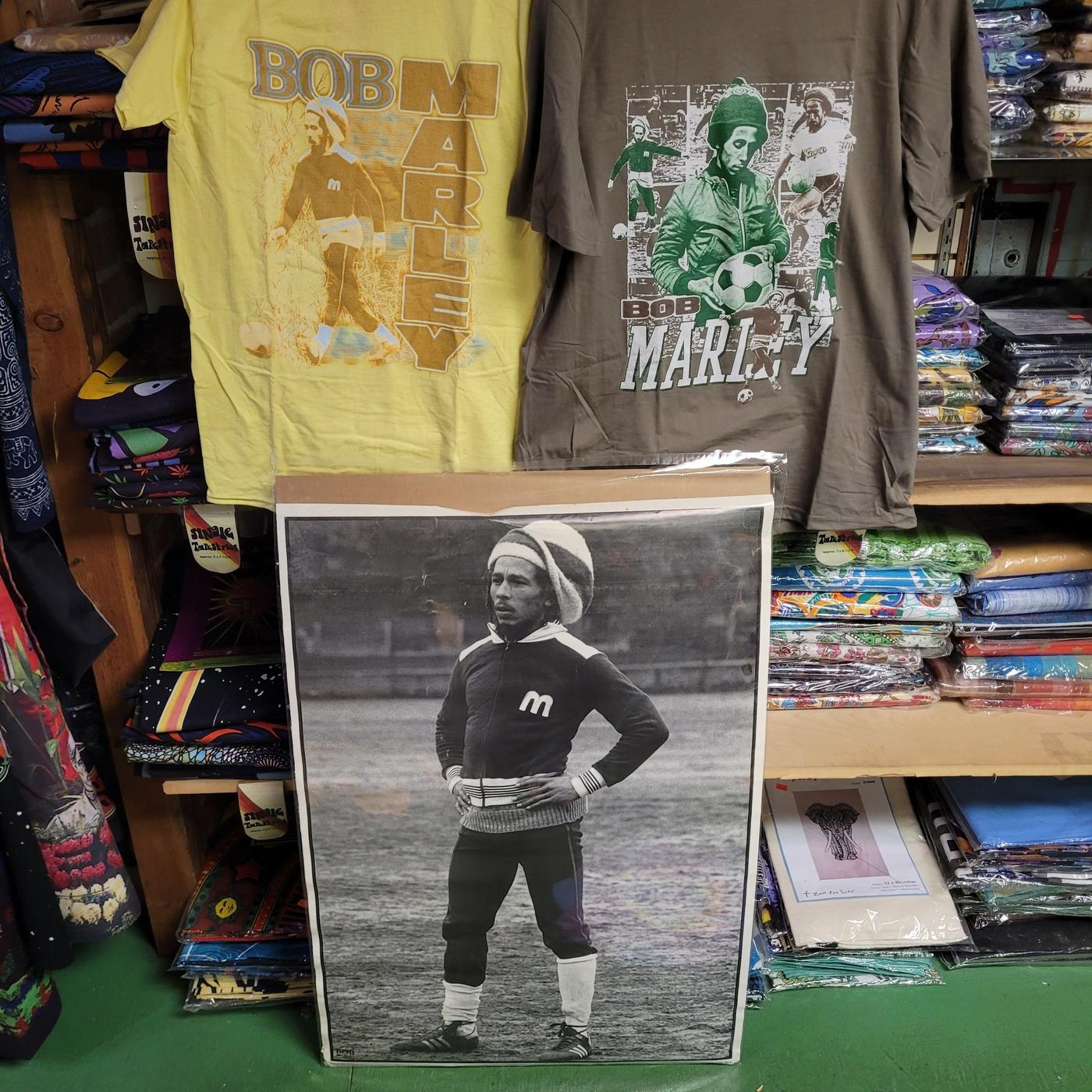 Bob Marley t-shirts and a poster above shelves of folded tapestries in packets.