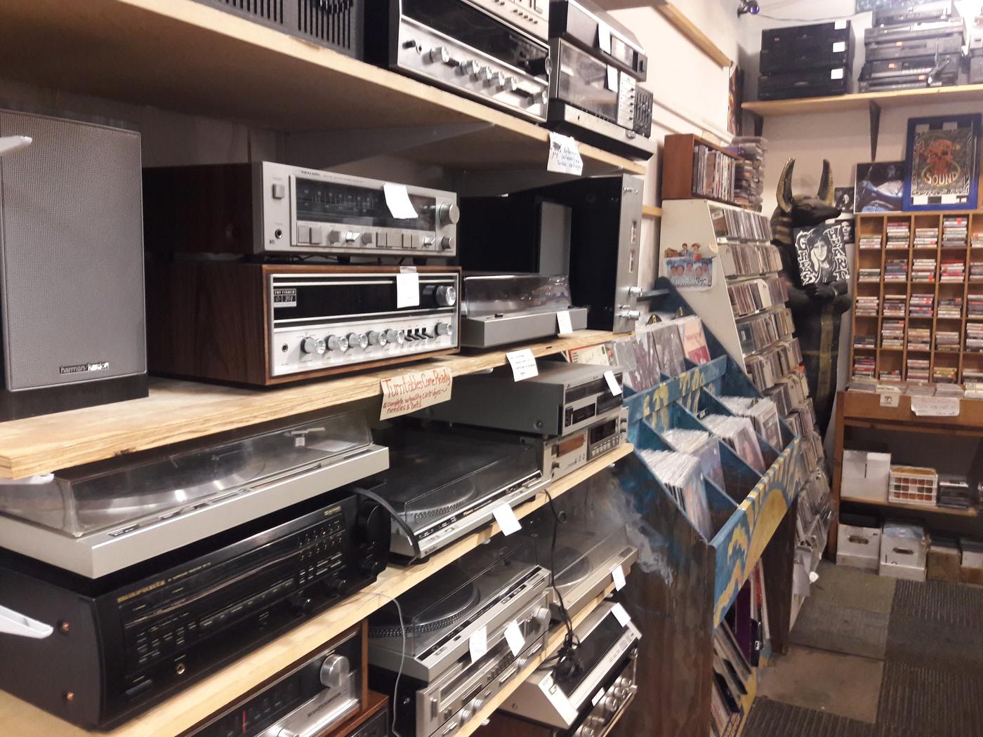 Shelves of turntables, receivers and tape decks for sale, with racks of CDs and cassettes alongside.